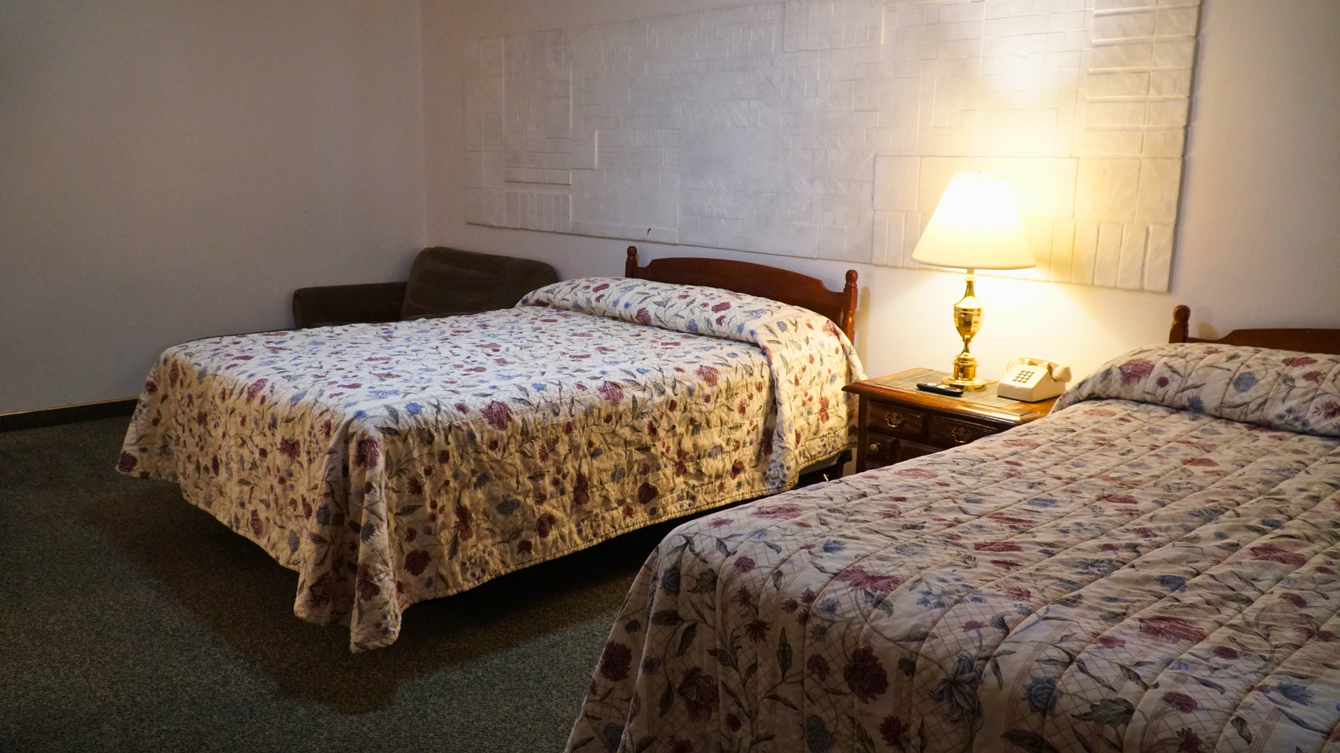 Hotel room with two floral-patterned beds and a lit bedside lamp on a nightstand