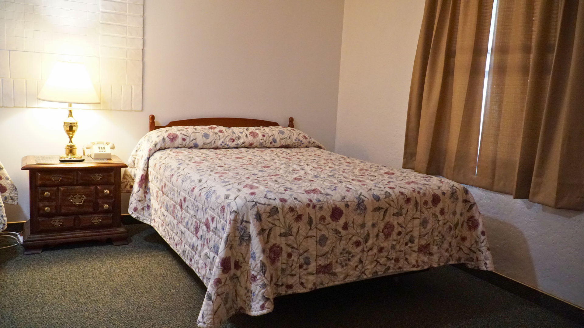 Cozy bedroom with floral bedspread, wooden nightstand, lamp, and beige curtains
