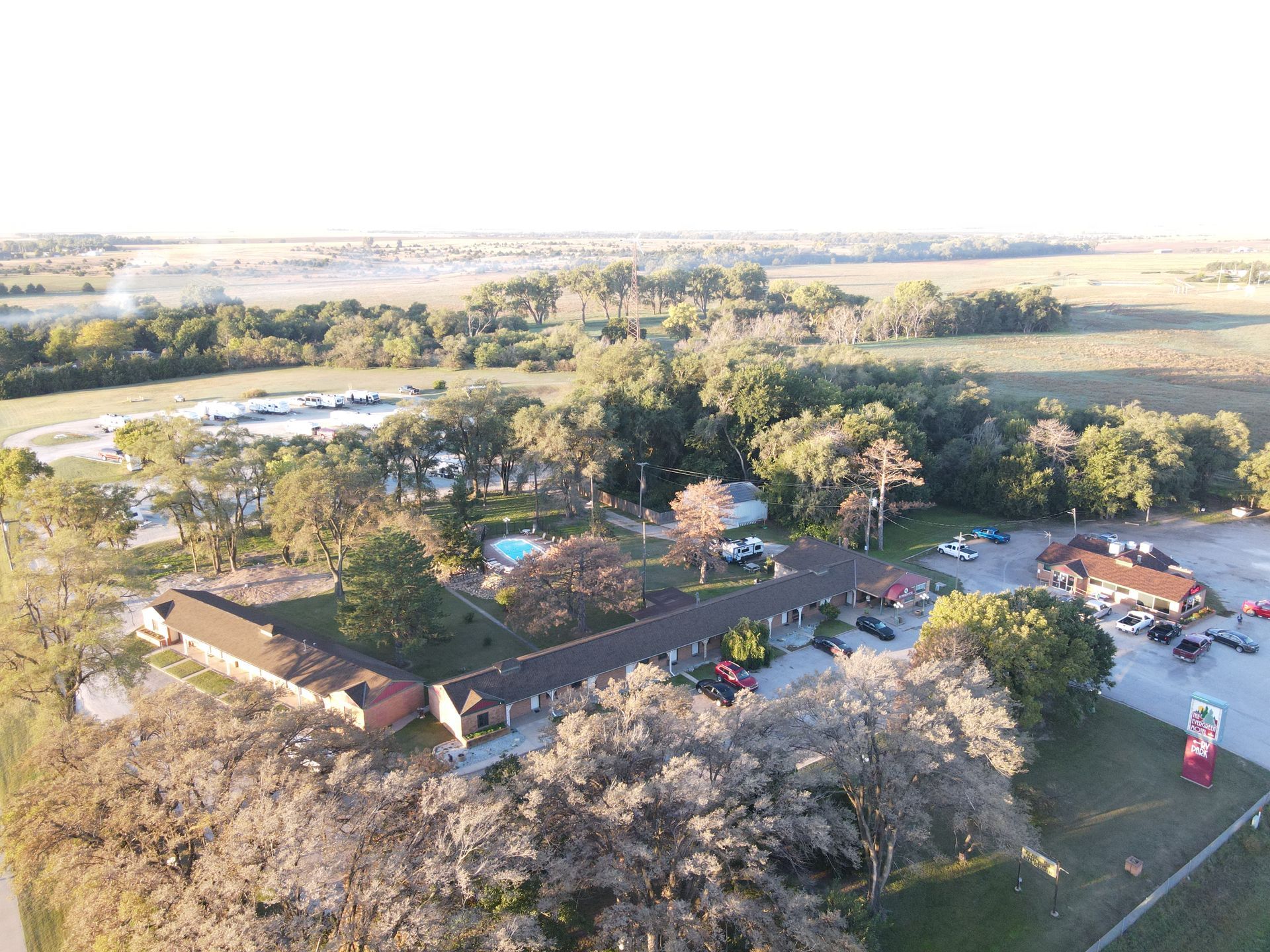 Aerial view of a rural park with trees, buildings, parking area, and open fields beyond.