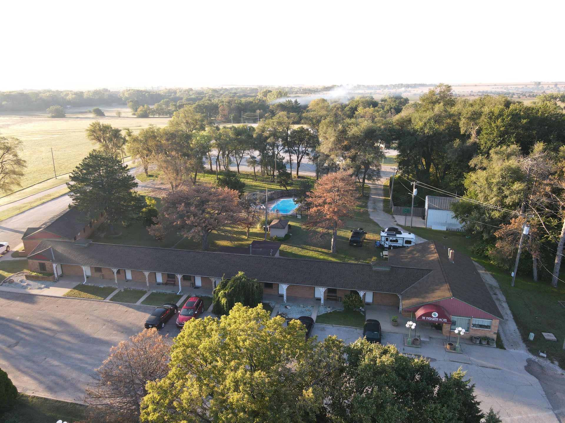 Aerial view of a park with trees, a playground, walking paths, and parked cars at the edge of a field