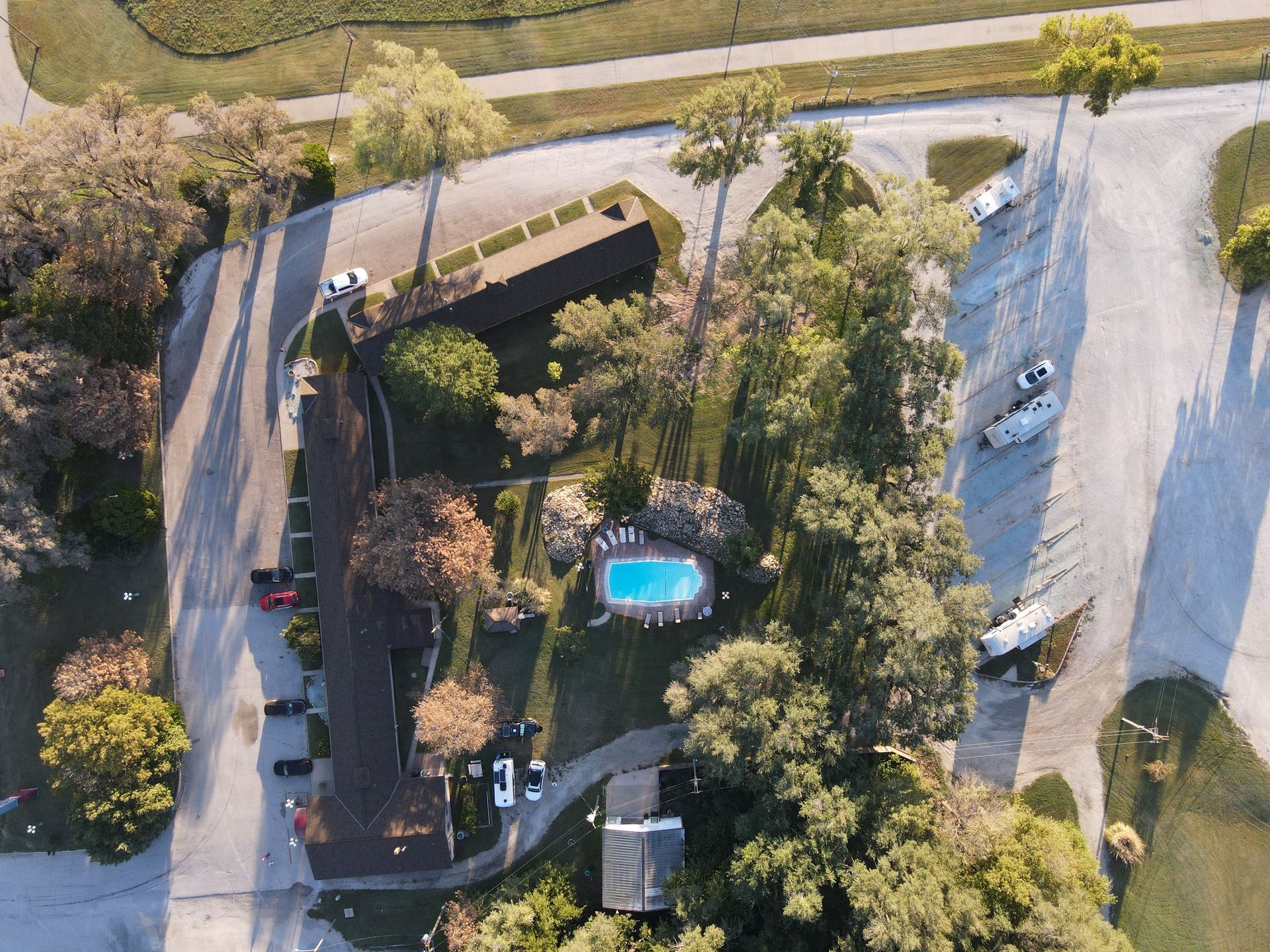 Aerial view of a motel with a small blue pool, trees, and a curving driveway by the road