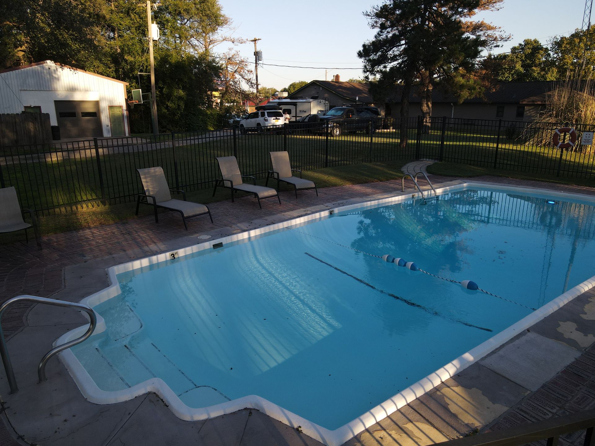 Motel swimming pool with lounge chairs and a fence in warm sunlight