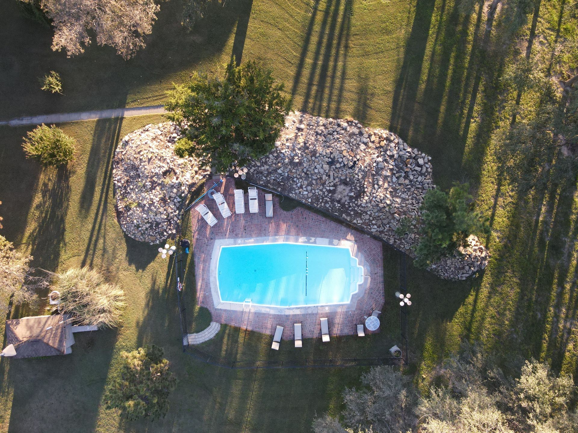 Aerial view of a pool with lounge chairs, trees, and long shadows at sunset