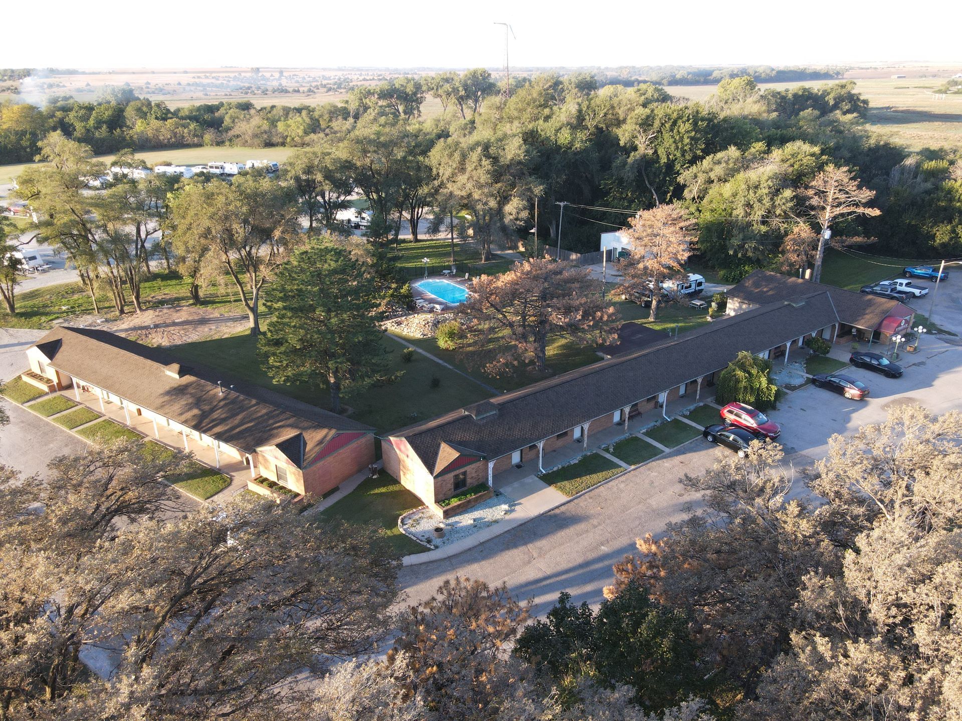 Aerial view of a motel with a pool, surrounded by trees and a parking lot