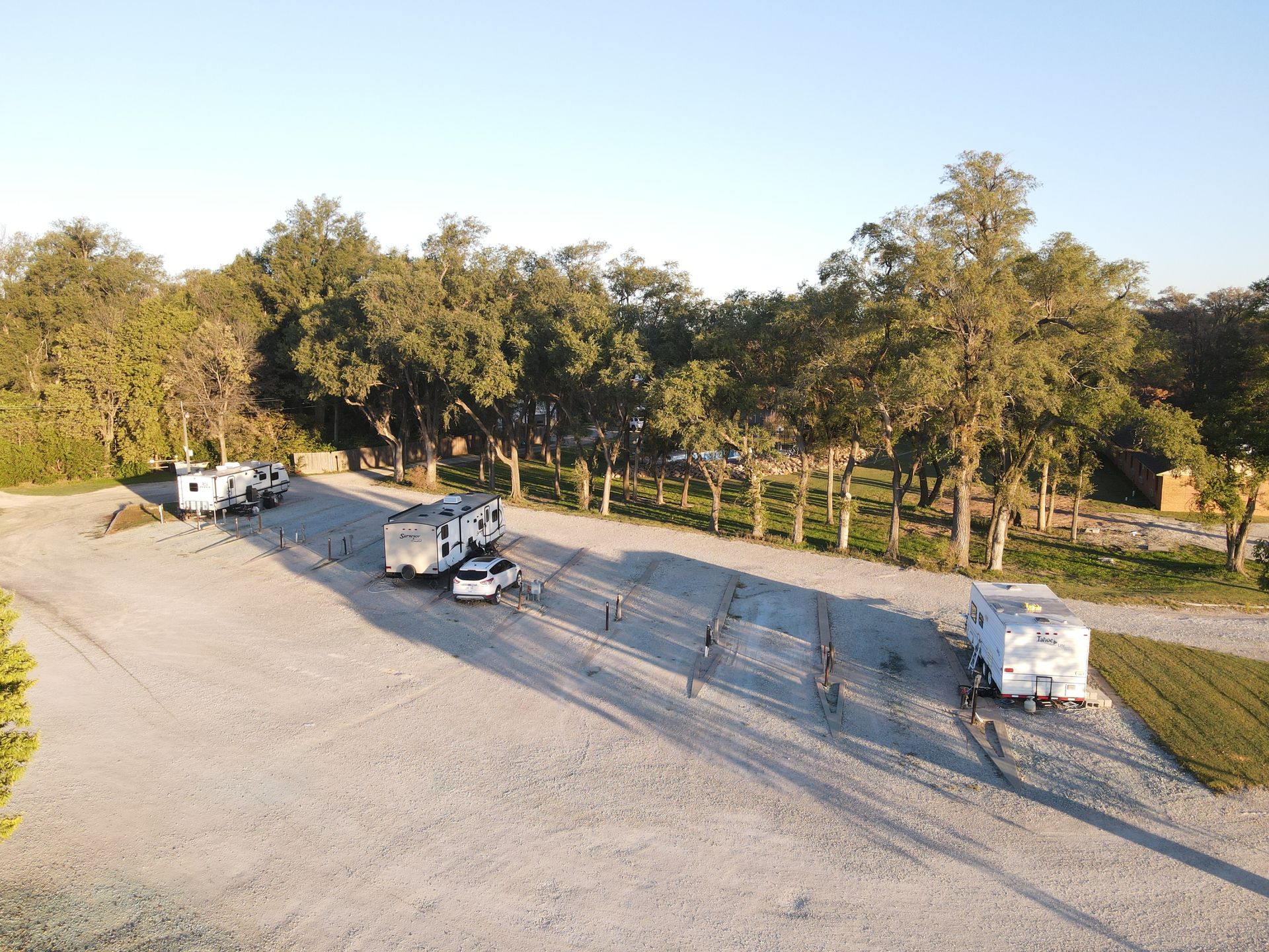 Parking lot with several RVs and vans beside a tree-lined road at sunset