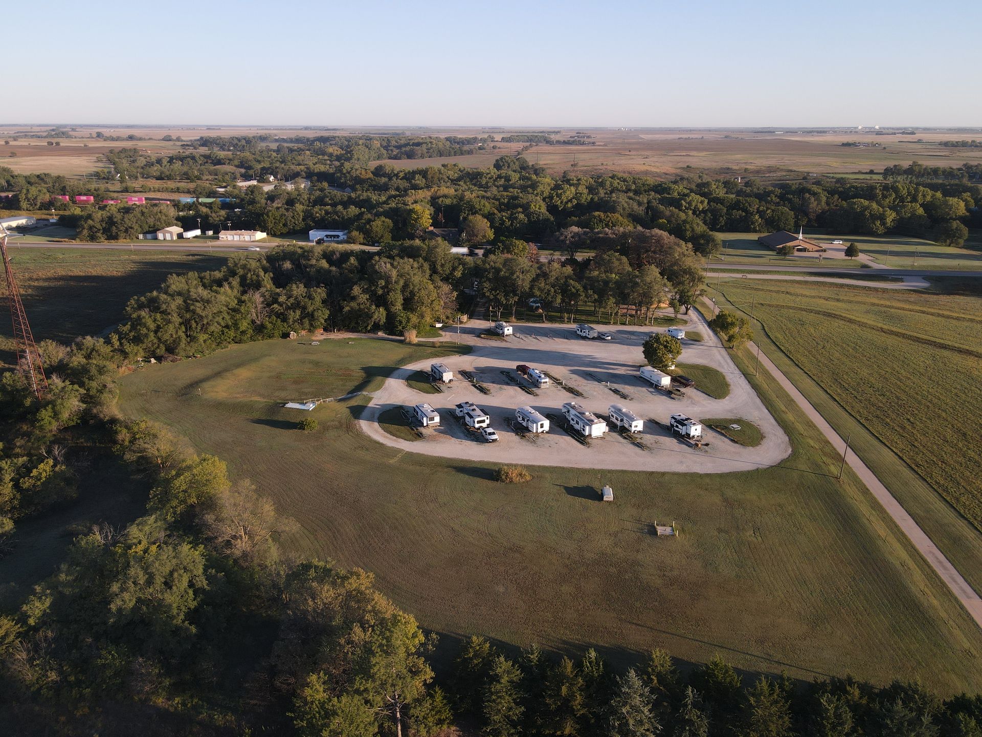 Aerial view of a rural campground with RVs parked in a loop amid fields and trees at sunset.