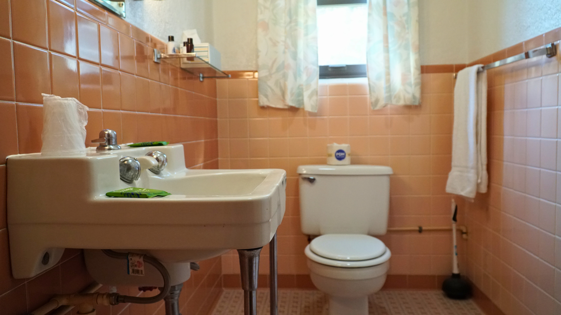 Small bathroom with orange tiled walls, a white sink, toilet, window, and towel rack.