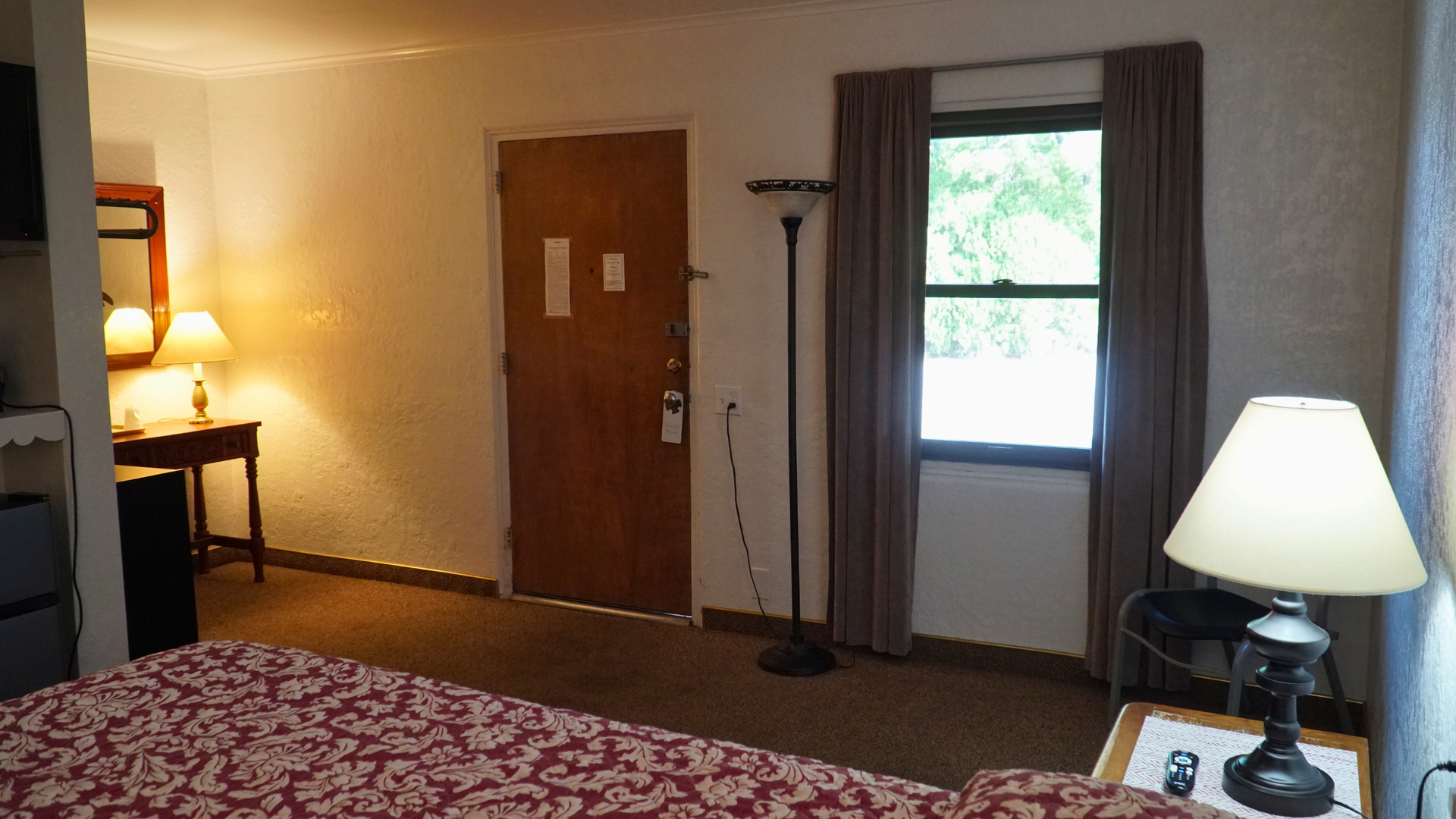 Hotel room interior with bed, lamp, closed door, and window with a view outside