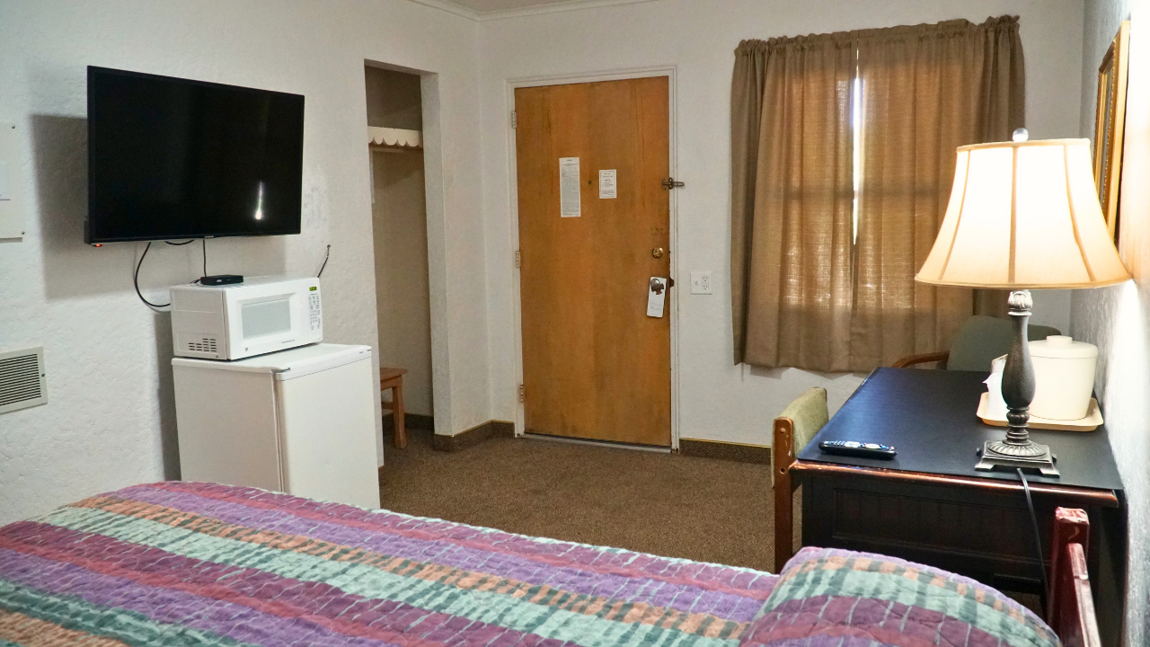 Motel room with bed, TV, mini fridge, desk lamp, and curtained window