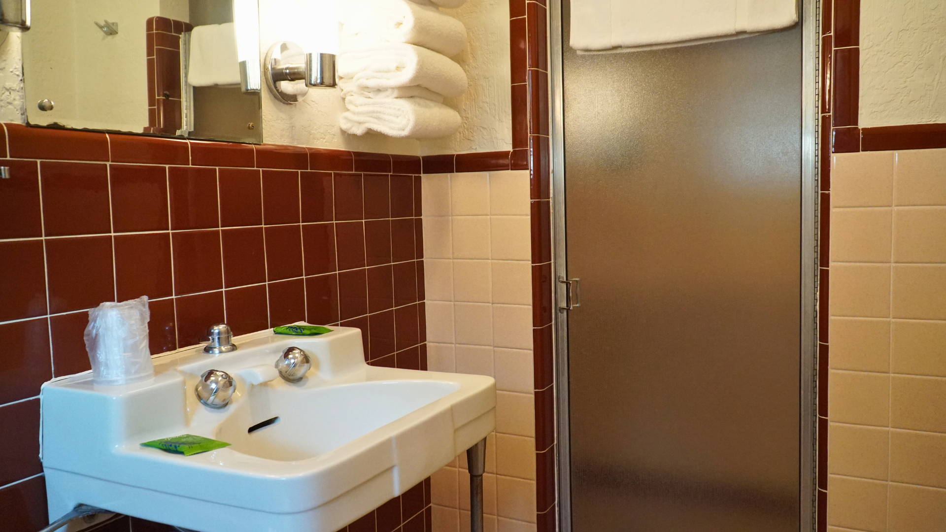 Small bathroom with a white sink, dark red tile, beige walls, and a frosted shower door