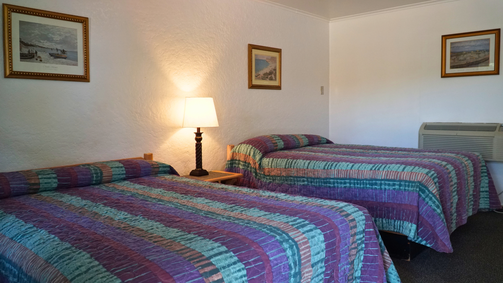 Hotel room with two beds, colorful bedspreads, lamp, and framed wall art