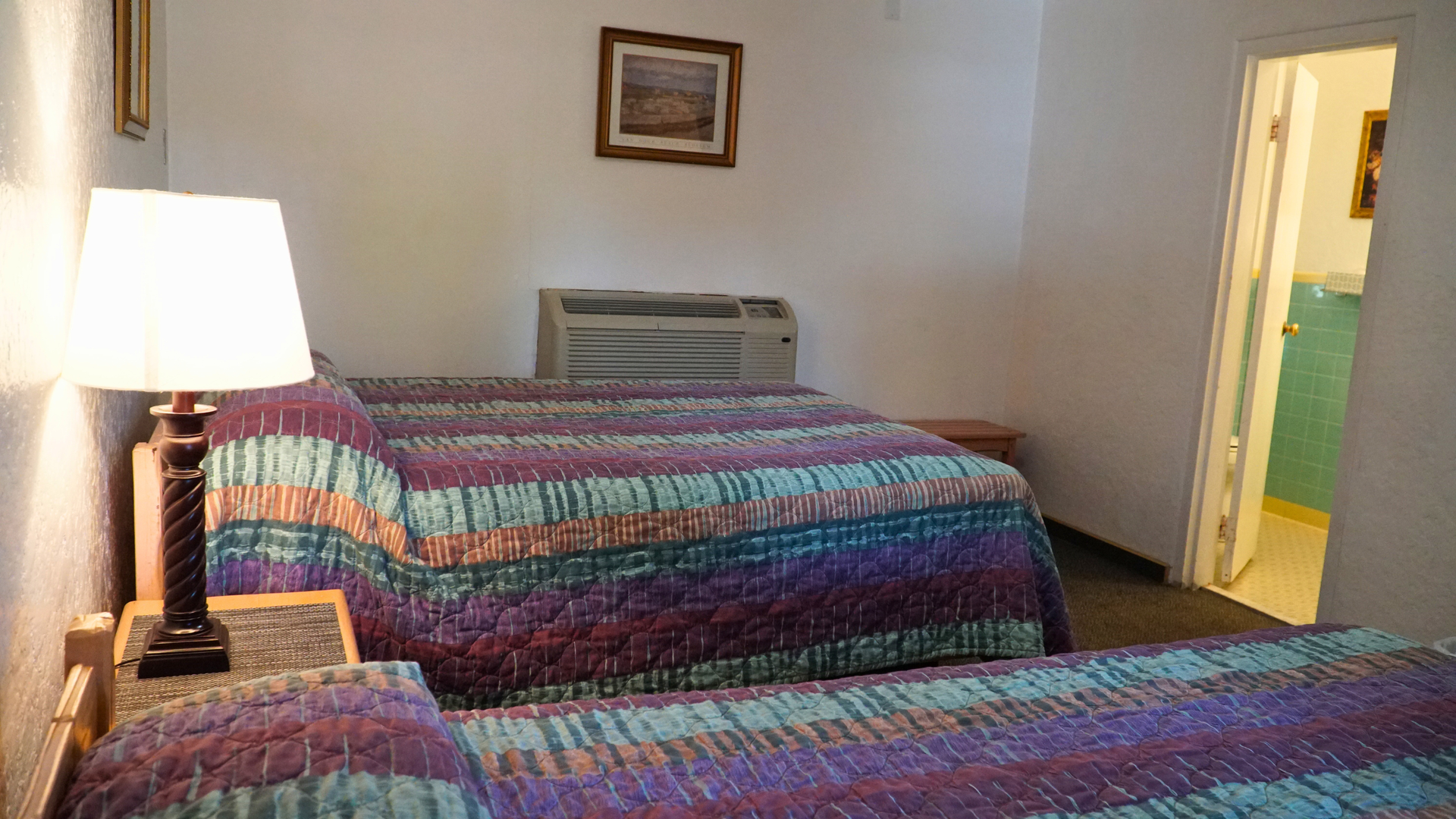 Hotel room with two double beds, a lit lamp, and an open doorway to a bathroom.