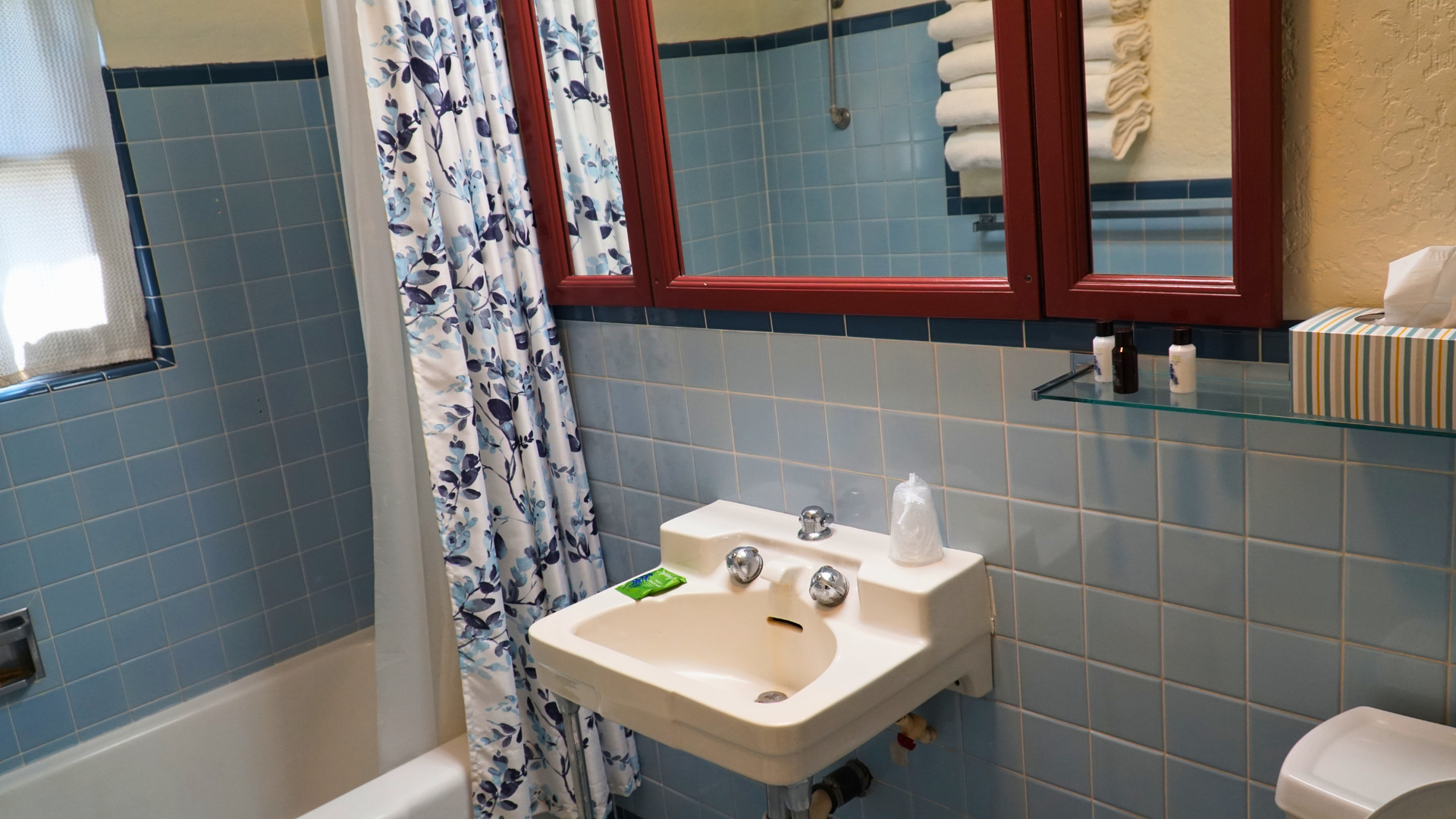 Small bathroom with blue tile, a sink, mirror cabinet, bathtub, and shower curtain.