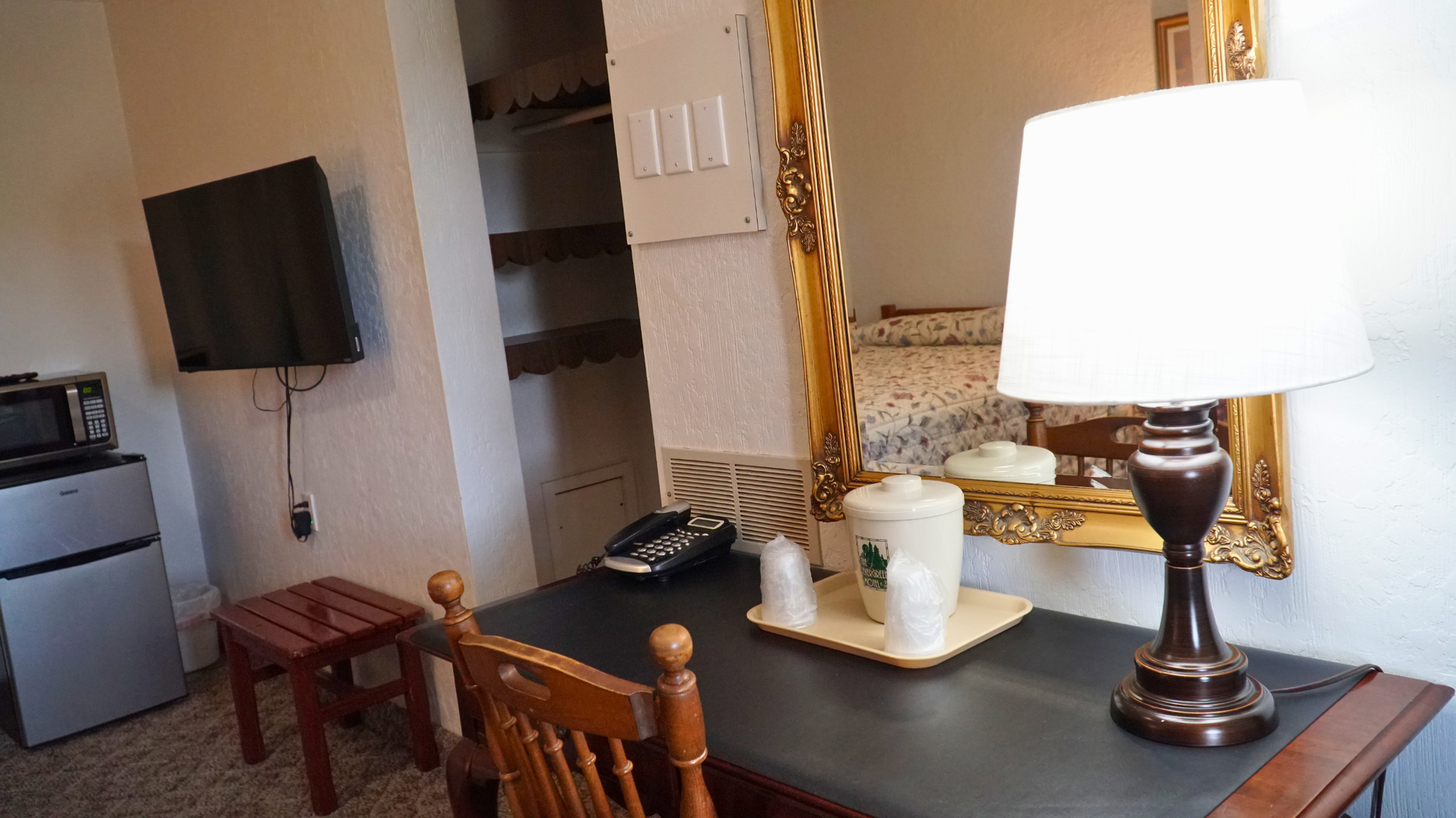 A desk with a lamp and cup beside a TV, mirror, and open closet in a small room.