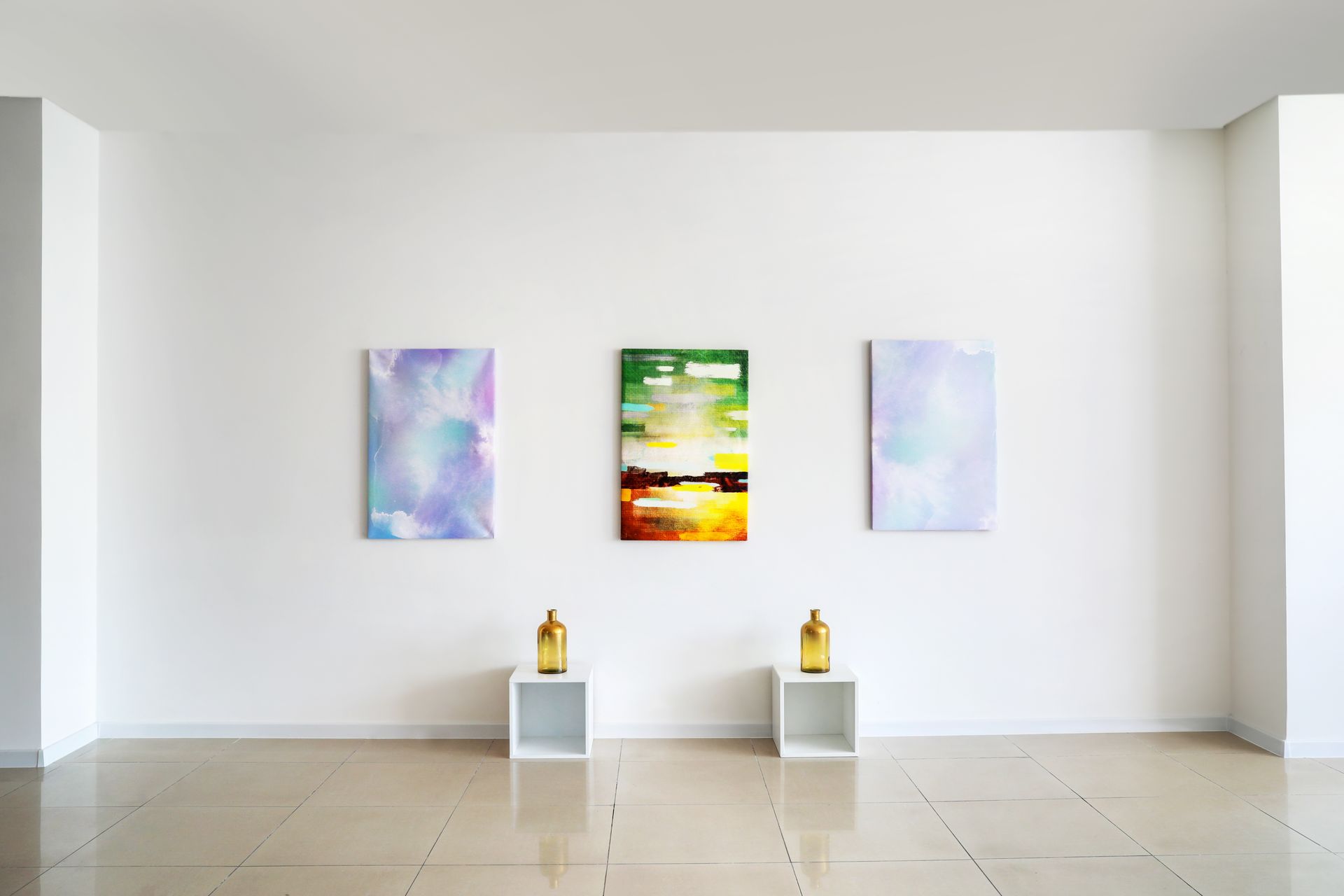 Minimalist gallery wall with three abstract paintings and two sculptures on pedestals in a bright white room