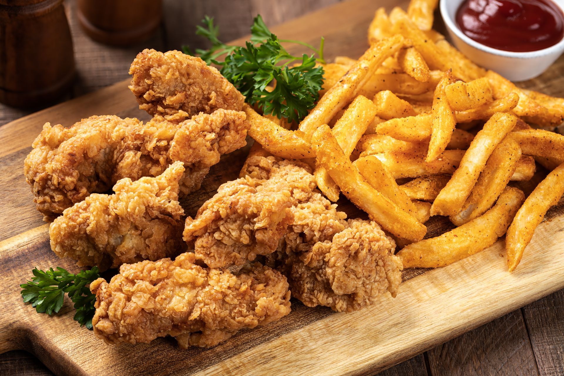 Fried chicken tenders with seasoned fries and ketchup on a wooden board