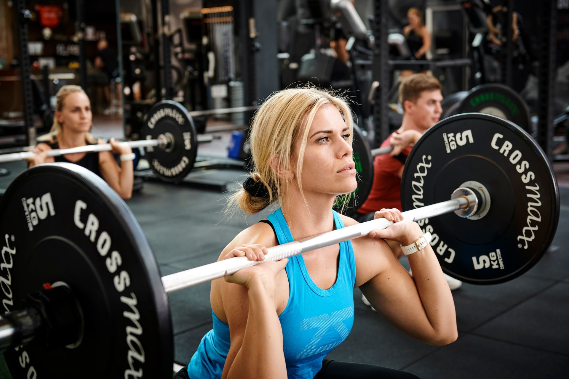 En mand løfter en vægtstang i et fitnesscenter, mens en anden mand ser på.