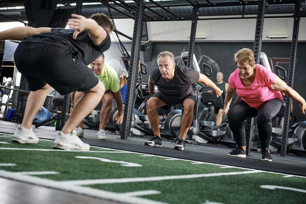 En gruppe mennesker laver squats i et fitnesscenter.