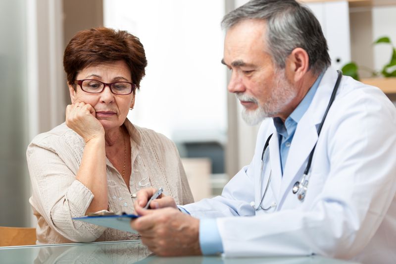 Doctor in white coat reviews clipboard with a patient; indoor setting.