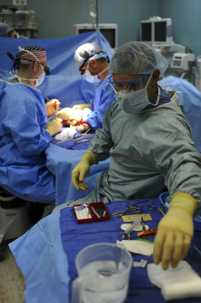 Medical team performing surgery in a sterile operating room, with instruments and tools on a blue draped table.
