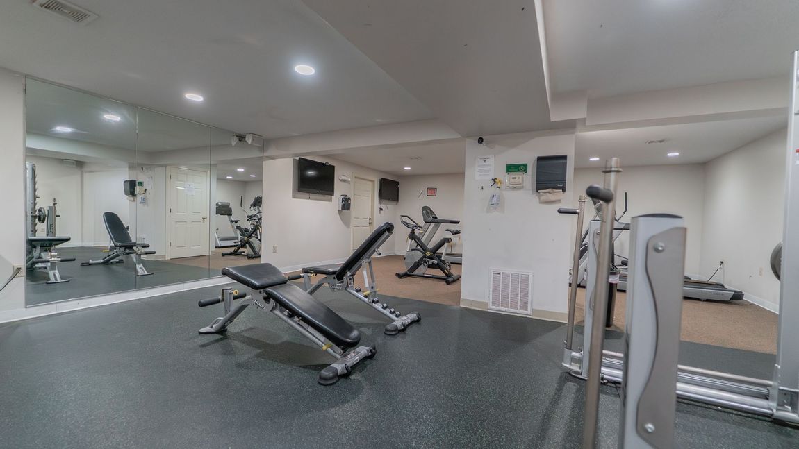 Gym interior with weight benches, exercise machines, mirrors, and a dark floor.