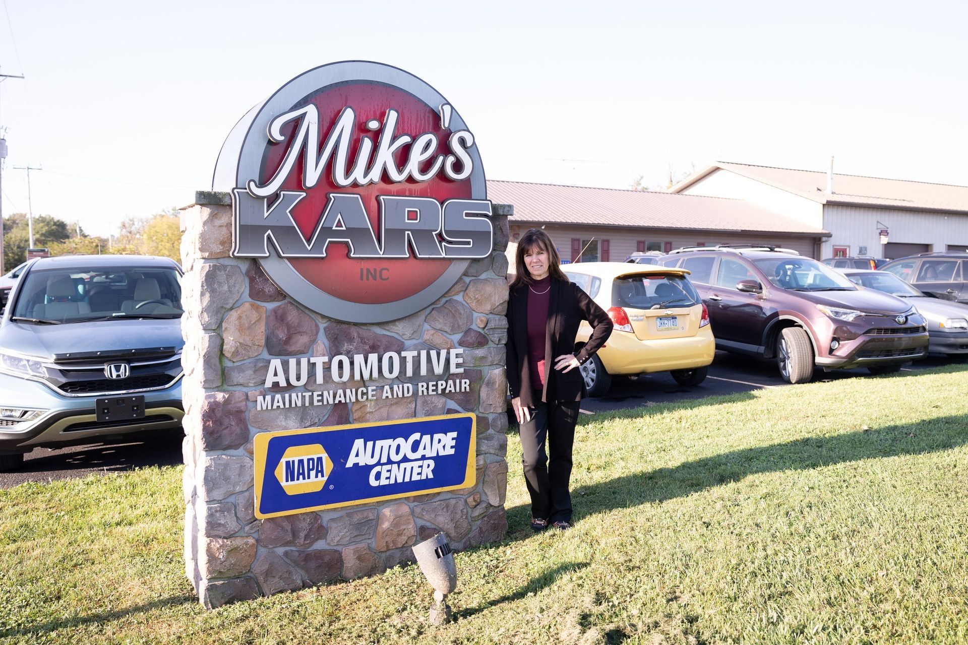 A woman stands in front of a mike 's kars automotive sign