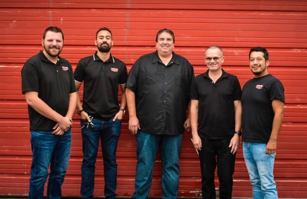 A group of men are standing in front of a red garage door.
