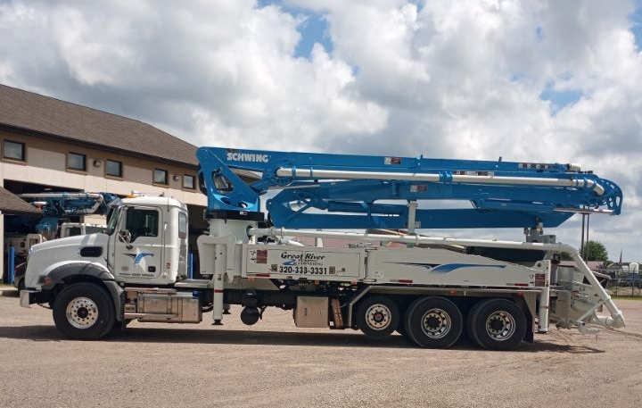 Blue concrete pump truck parked outside a warehouse