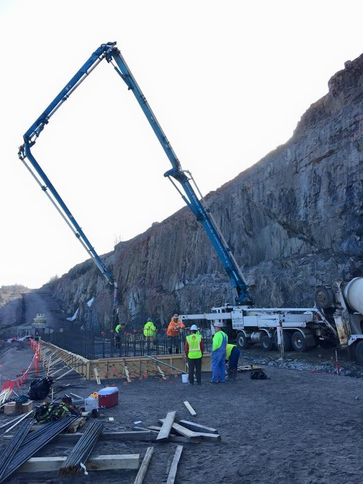 Construction crew with blue concrete pump truck pouring at a cliffside site