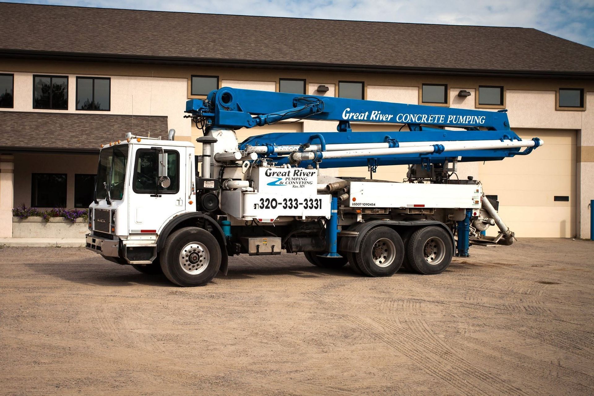 Blue concrete pump truck parked in front of a beige building with garage doors