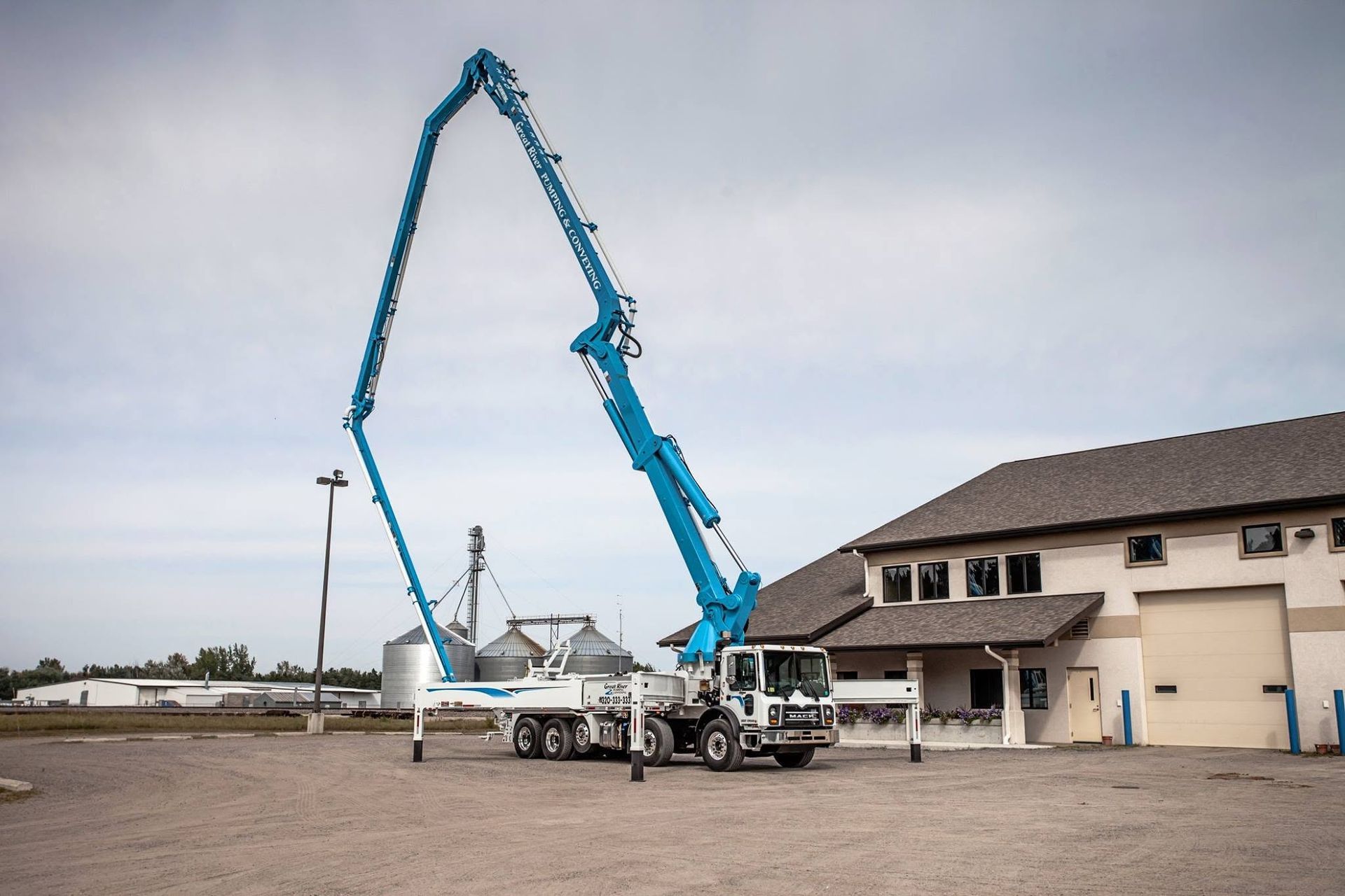 Blue concrete pump truck extended over a building under construction on a gravel lot