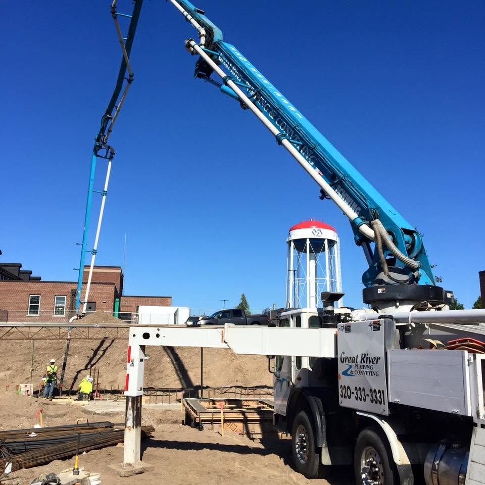Construction truck with blue crane lifting materials beside a brick building under a clear blue sky