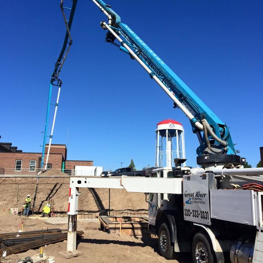 Blue boom crane truck lifting a concrete pile at a construction site under a clear sky.