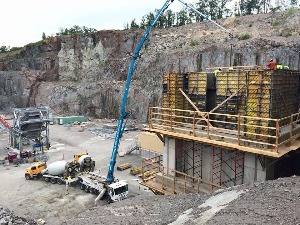 Construction site with concrete pump truck pouring concrete into a building framework beside a rocky cliff
