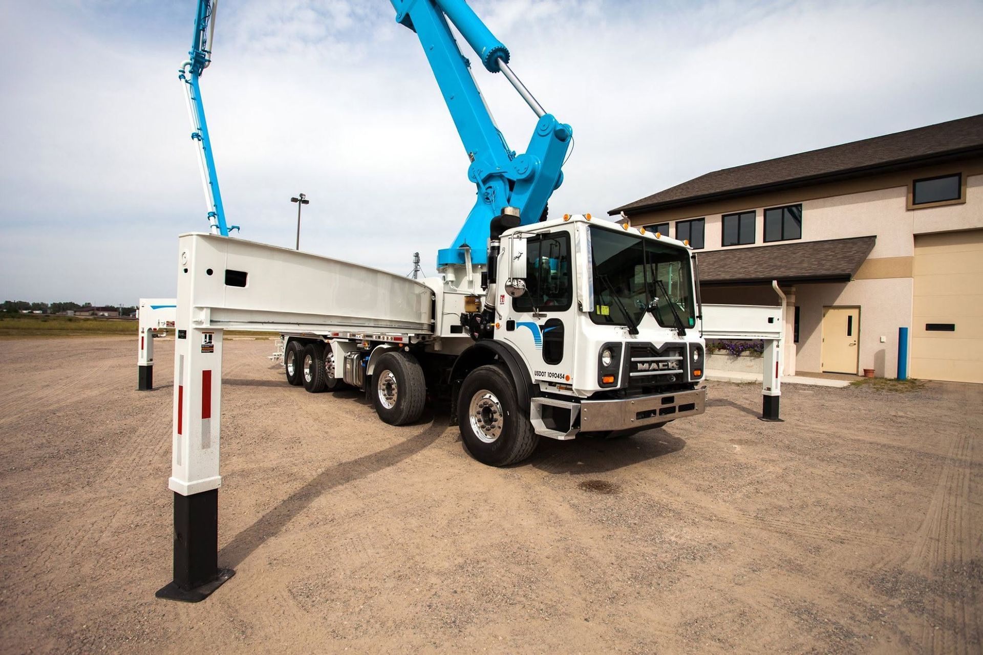 Blue crane truck lifting a white utility trailer in a parking lot beside a beige building