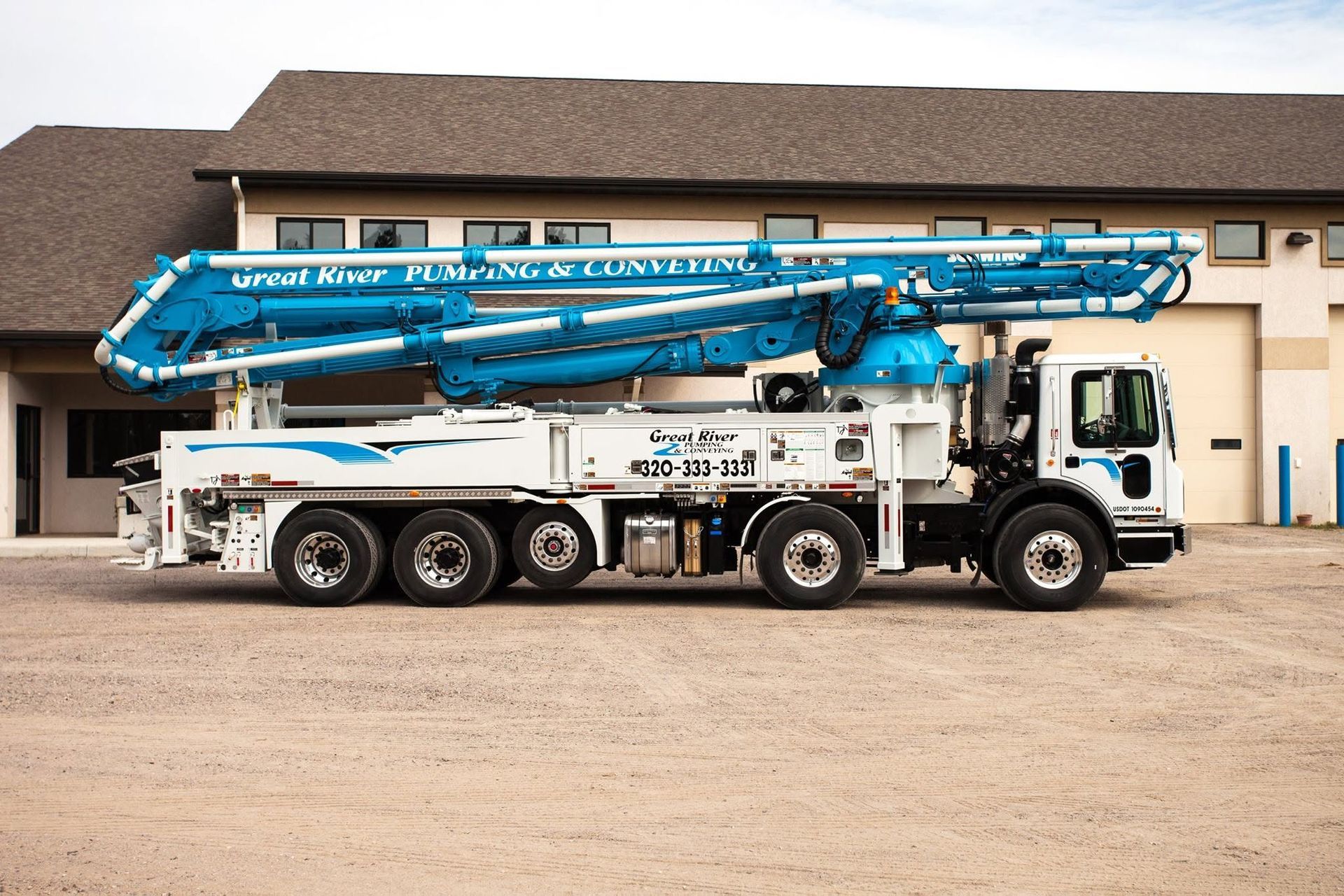 Blue concrete pump truck parked outdoors beside a beige building