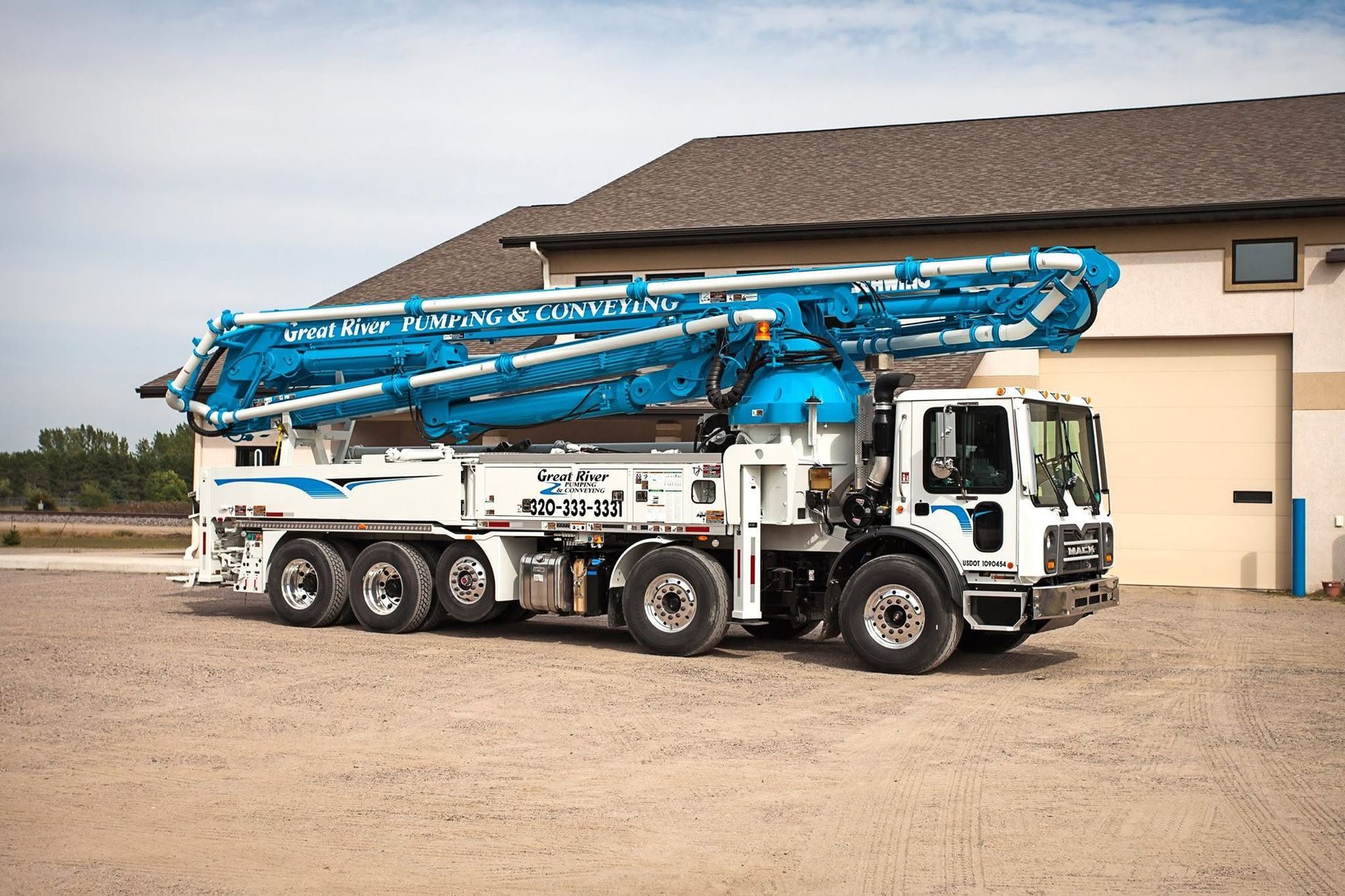 Blue and white concrete pump truck parked outside a beige industrial building