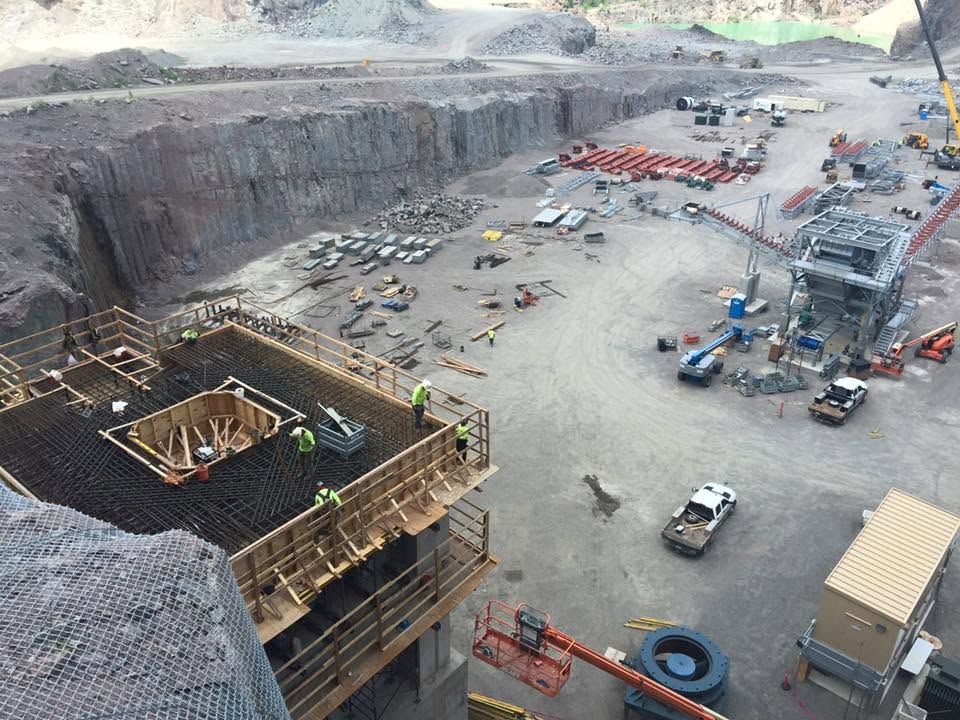 Large open-pit construction site with heavy machinery, excavators, trucks, and a concrete structure in the foreground