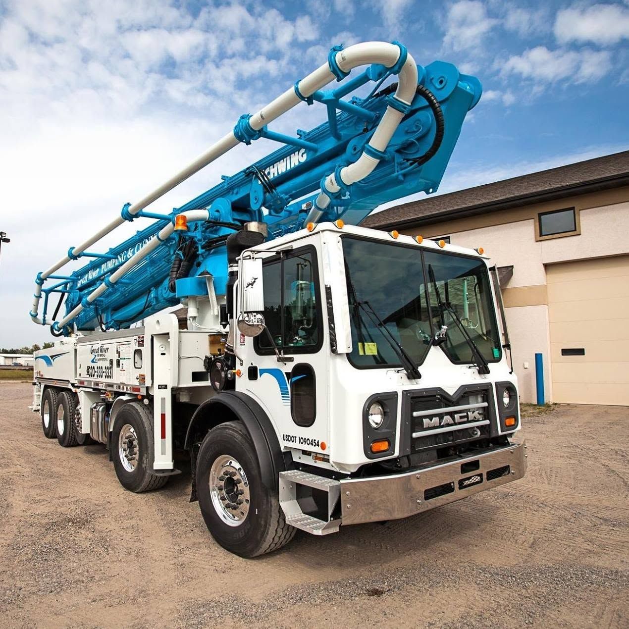 White concrete pump truck with blue boom parked outdoors near a building