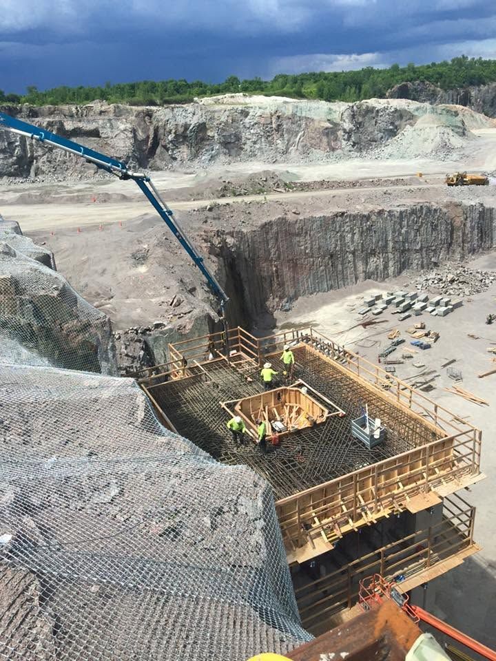 Open-pit mine with a concrete chute, workers, and scaffolding in a rocky excavation