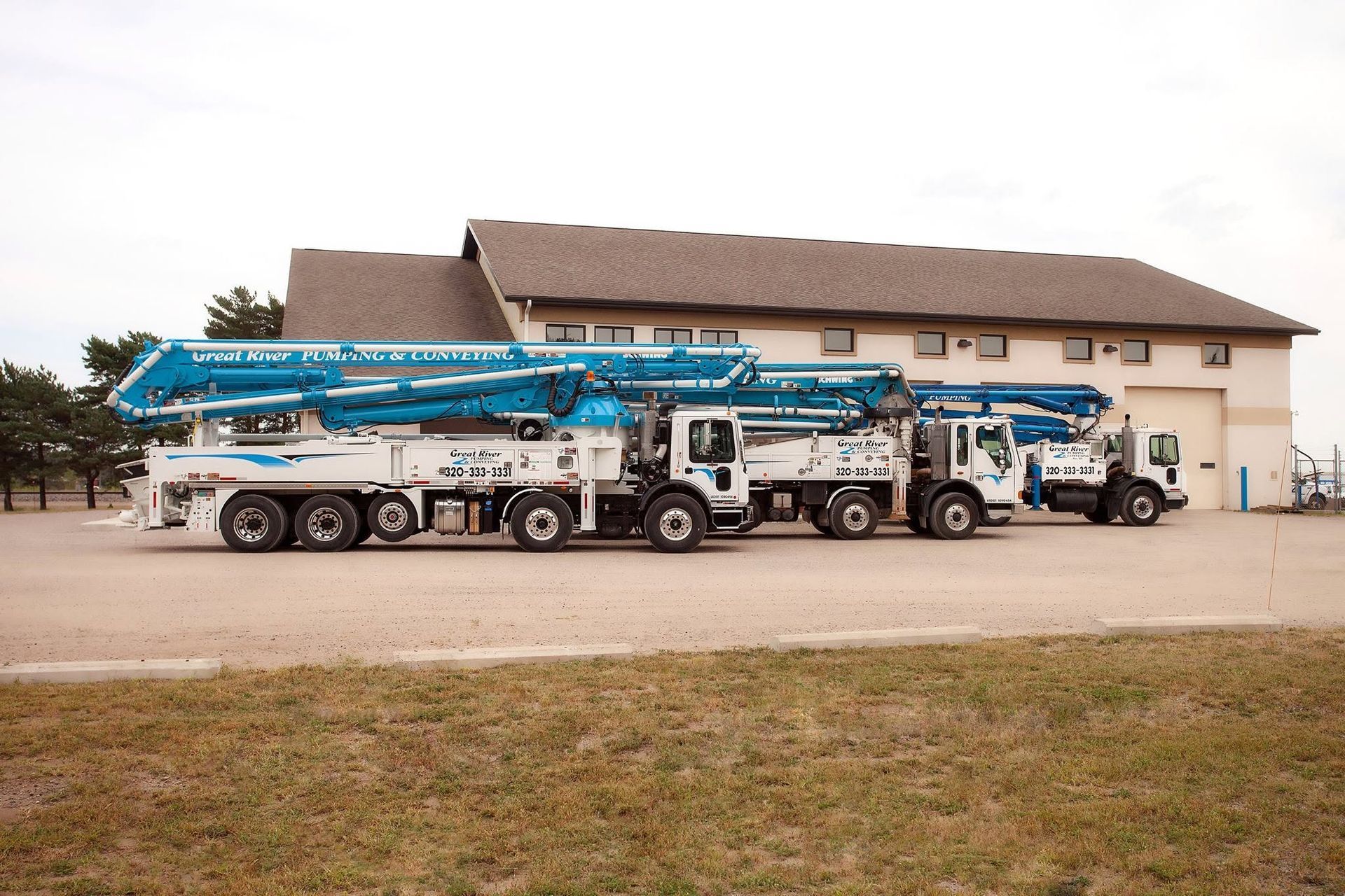 Three blue-and-white concrete pump trucks parked in front of a beige house with a large garage