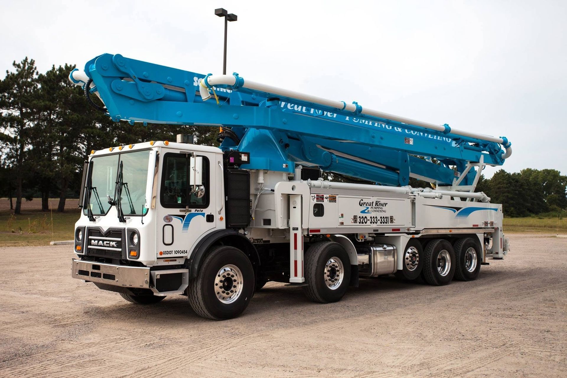 Blue and white concrete pump truck parked on a gravel lot under a cloudy sky