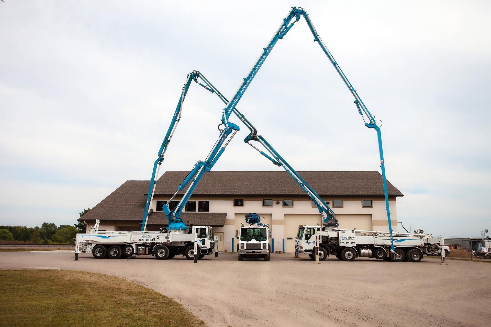 Two blue concrete pumps pouring over a house under construction with workers on-site