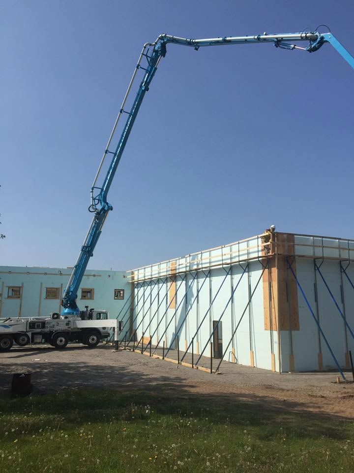 Concrete pump truck extending boom to pour concrete near a white building under a blue sky