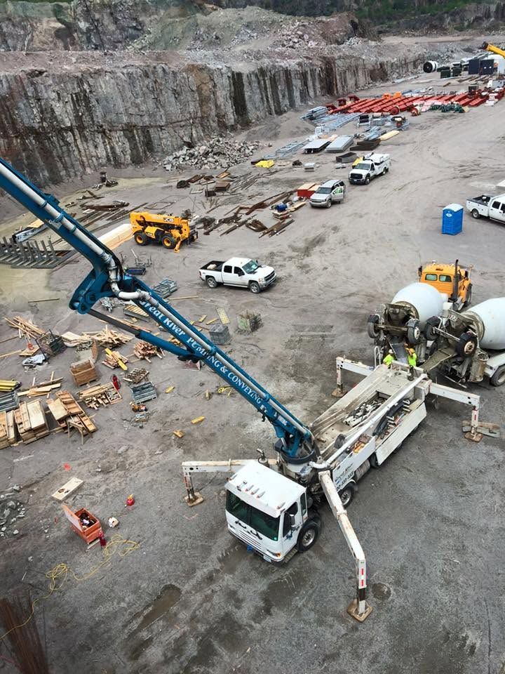 Concrete pump truck pouring at a construction site with trucks, equipment, and excavator nearby