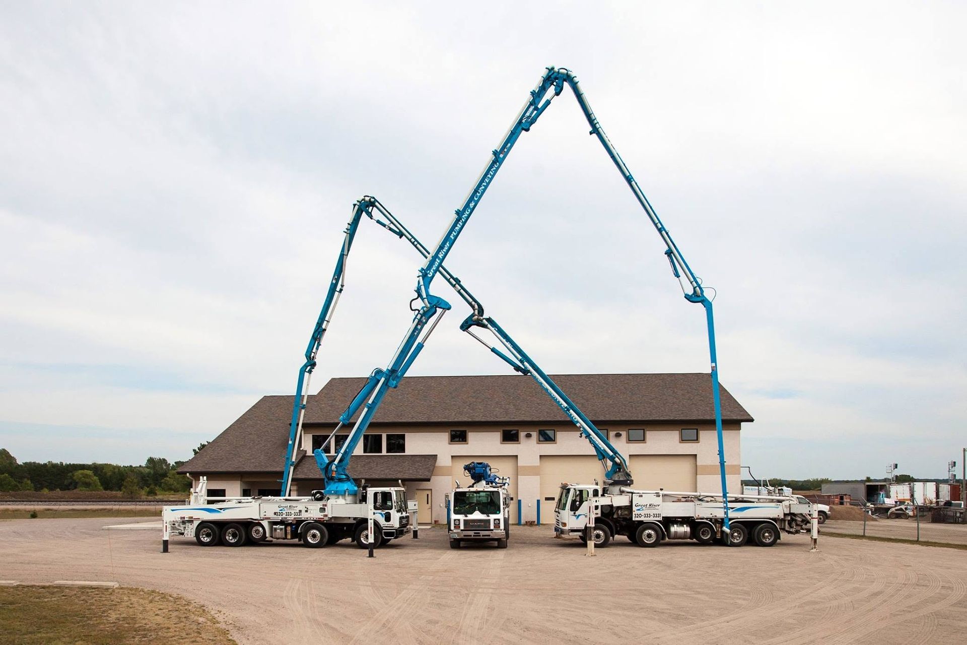 Two blue concrete pump trucks extending booms over a house under construction