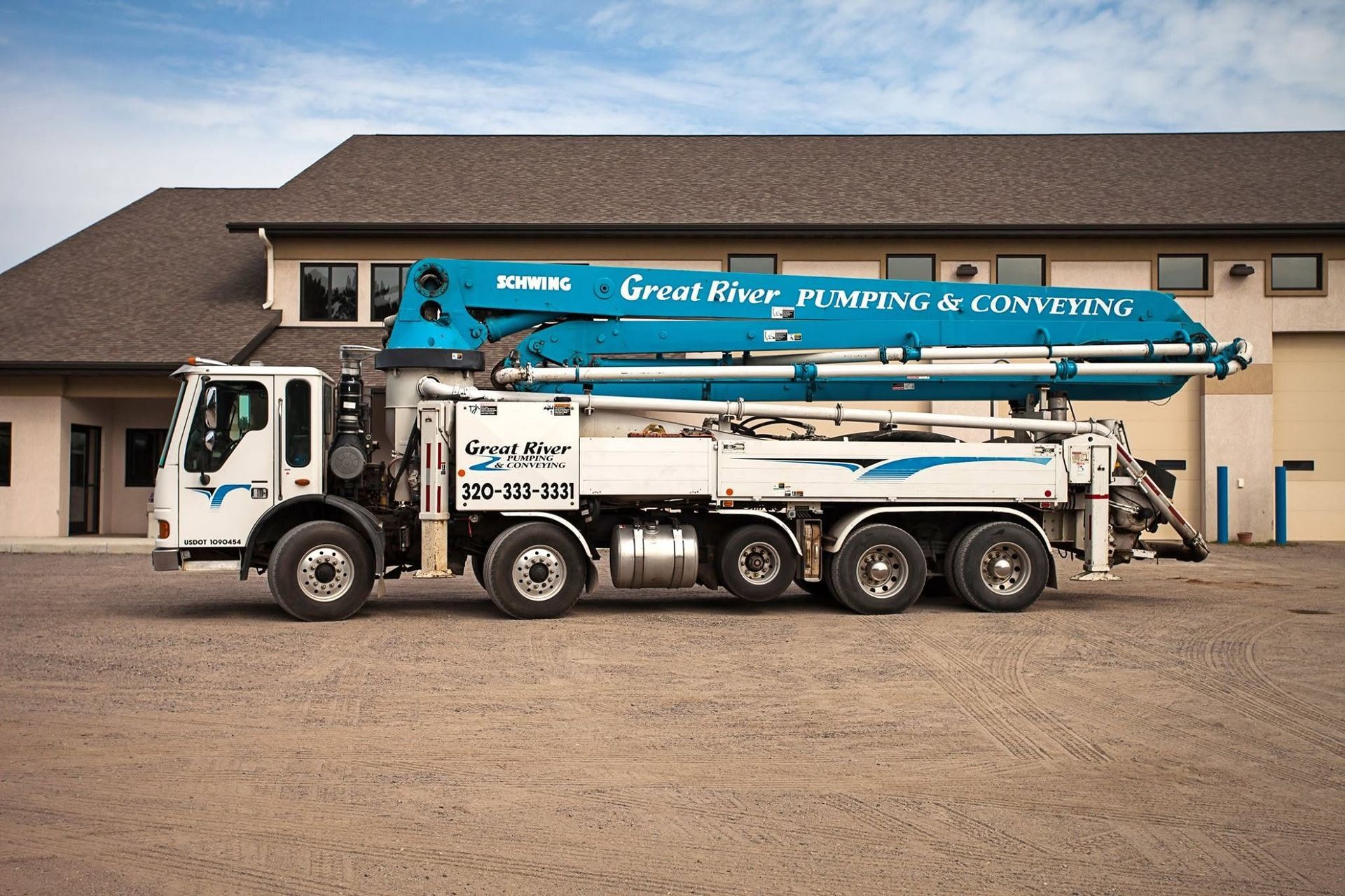 White concrete pump truck parked in front of a large building under a blue sky