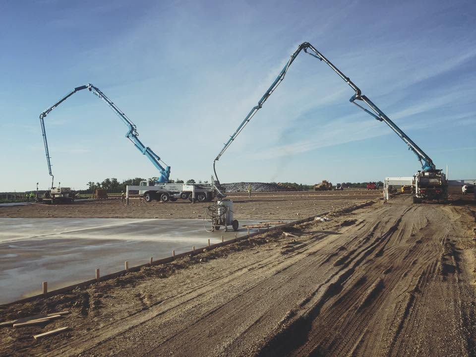 Two concrete pump booms pouring at a large construction site under a clear blue sky