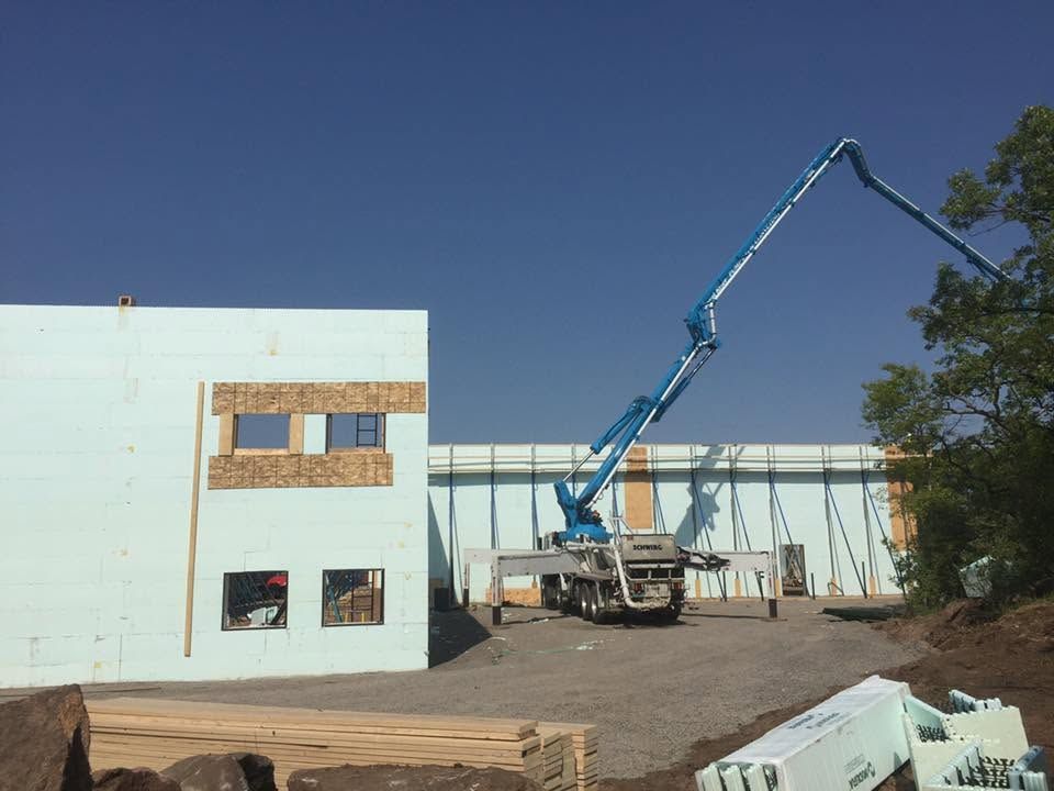 Construction site with a blue concrete pump truck beside a partially built white structure.