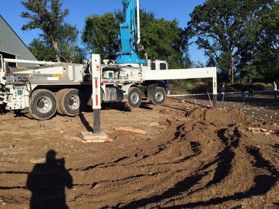 White crane truck on muddy construction site with blue boom and trees in the background